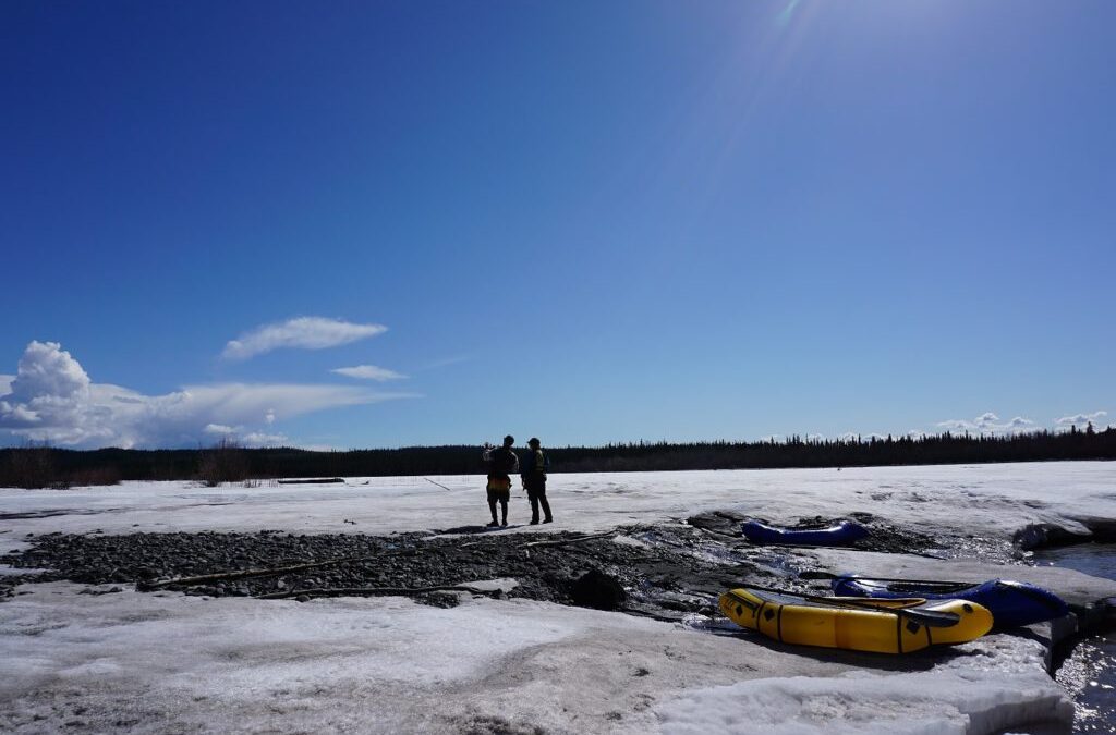 Two people by icy river with kayaks.